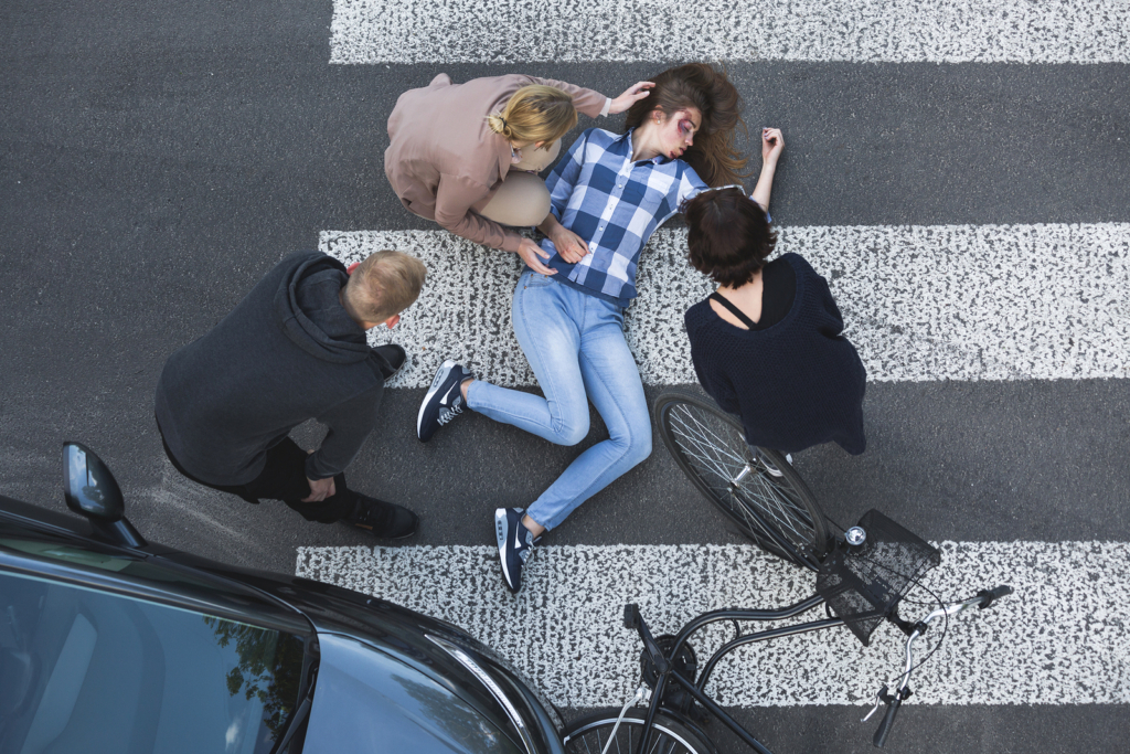 An injured person lies in the street after being hit by a car.