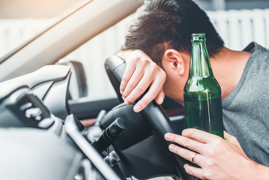 Drunk man driving a car on the road holding bottle beer