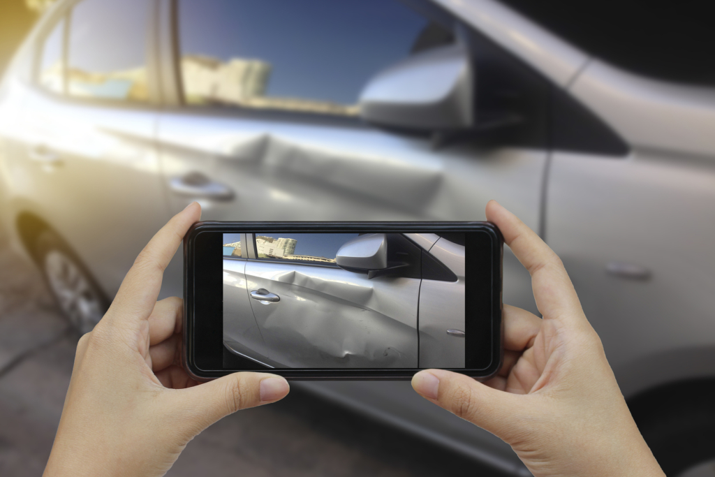 Hand holding smart phone takes a photo at the scene of a car crash and accident for insurance.