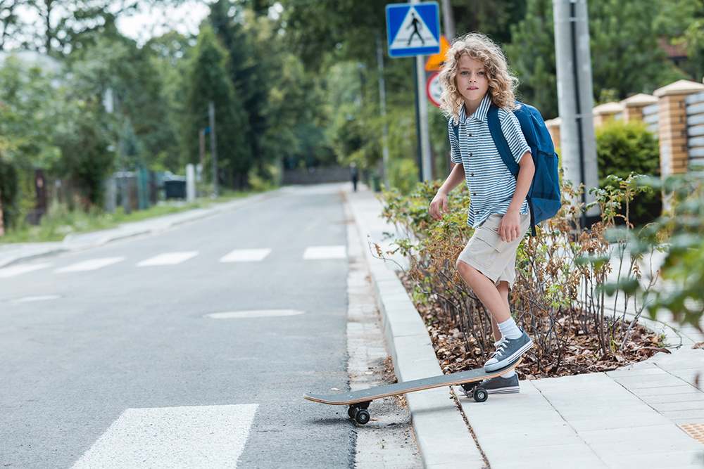 School kid with a skateboard at the side of a road