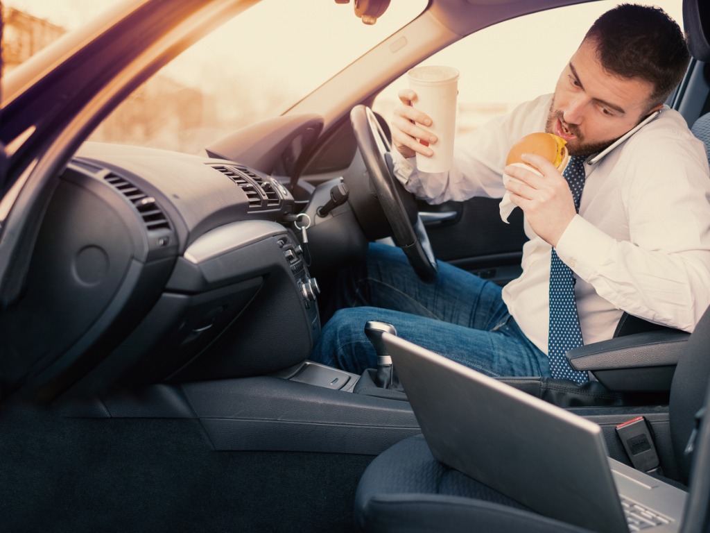 Man eating an hamburger and working seated his car picture id944651980